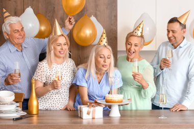 Mutfaktaki doğum günü partisinde arkadaşlarıyla dilek tutan olgun bir kadın.