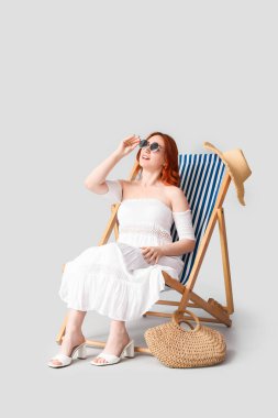 Güneş gözlüklü genç bir kadın arka planda iskemlede dinleniyor.