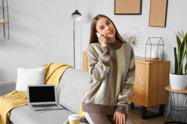 Evde cep telefonuyla konuşan genç bir kadın.