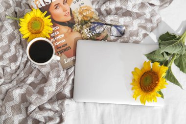 Güzel ayçiçekleri, bir fincan kahve, gözlük, dergi ve kumaş arka planda modern dizüstü bilgisayar.