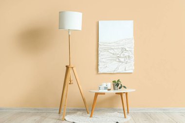 Boya, küçük masa ve bej duvarın yanında standart lamba.