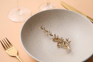 Bej masa üzerinde altın yapraklar ve çatal bıçak takımı olan zarif bir masa, yakın plan.