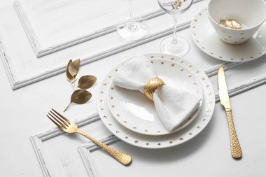 Beyaz ahşap arka planda altın yapraklı ve çatal bıçaklı zarif bir masa.