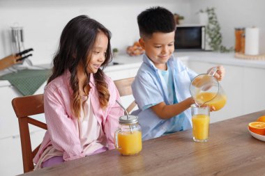 Küçük Asyalı çocuklar mutfaktaki masada sürahide taze narenciye suyu dolduruyorlar.