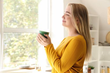 Mutfakta bir fincan sıcak çayla genç bir kadın.