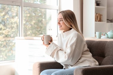 Bir fincan sıcak çayla mutfakta oturan genç bayan.