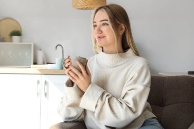 Bir fincan sıcak çayla mutfakta oturan genç bayan.