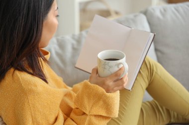 Oturma odasında kanepede oturmuş kitap okuyan Asyalı güzel bir kadın.