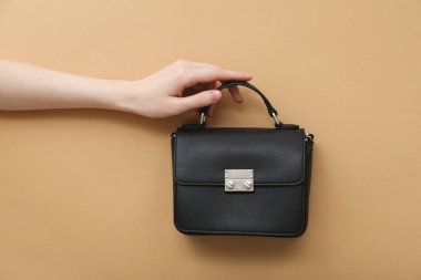 Kahverengi arka planda siyah çantalı bir kadın.