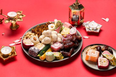 Kırmızı zemin üzerinde mum ve farklı tabaklar bulunan Diya lambaları. Divaly kutlaması