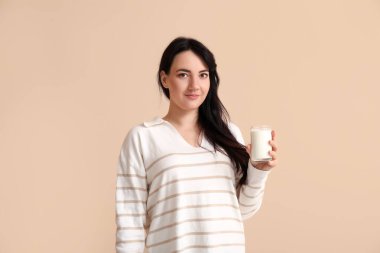 Bej arka planda bir bardak sütü olan güzel genç bir kadın.