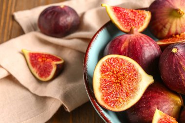 Kahverengi ahşap arka planda olgun taze incirlerle dolu bir kâse.