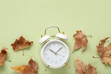 Yeşil zemin üzerinde sonbahar yaprakları olan çalar saat