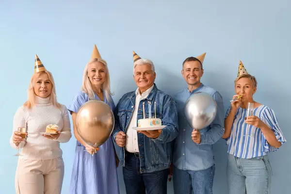 Mature people with cake and balloons celebrating Birthday on blue background