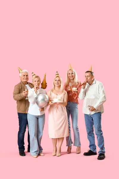 Mature people with cake and champagne celebrating Birthday on pink background