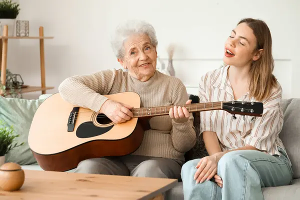 Young woman and her grandmother playing guitar at home