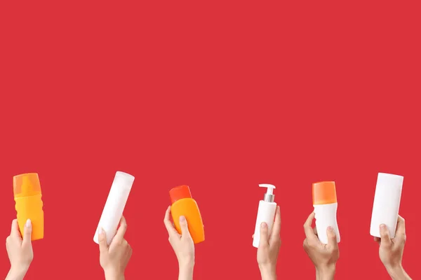 Female hands with bottles of sunscreen cream on red background
