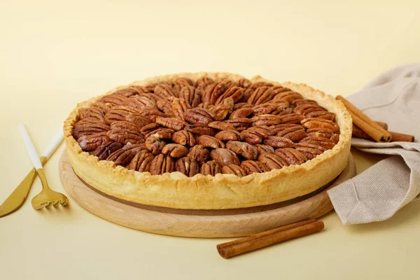 Wooden board with tasty pecan pie on yellow background