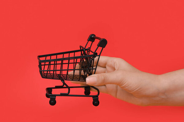 Female hand with small shopping cart on red background
