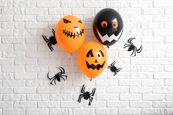 Different Halloween balloons and paper spiders hanging on light brick wall in room