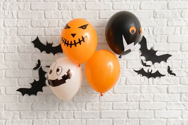Different Halloween balloons and paper bats hanging on light brick wall in room