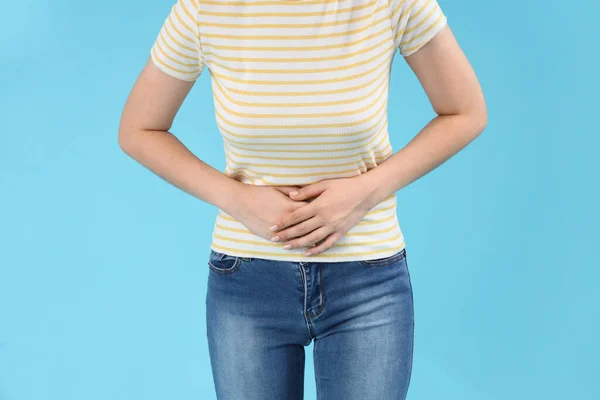 stock image Young beautiful woman suffering from abdominal pain on blue background, closeup