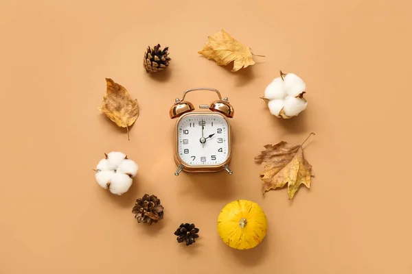 Alarm clock with fallen leaves, fir cones, pumpkin and cotton flowers on beige background
