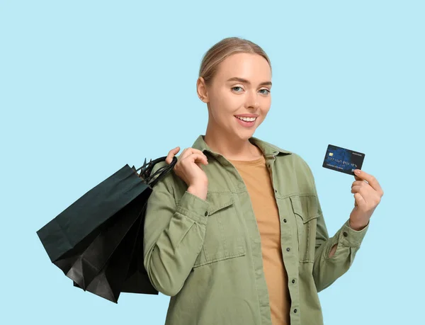 Pretty young woman with credit card and shopping bags on blue background