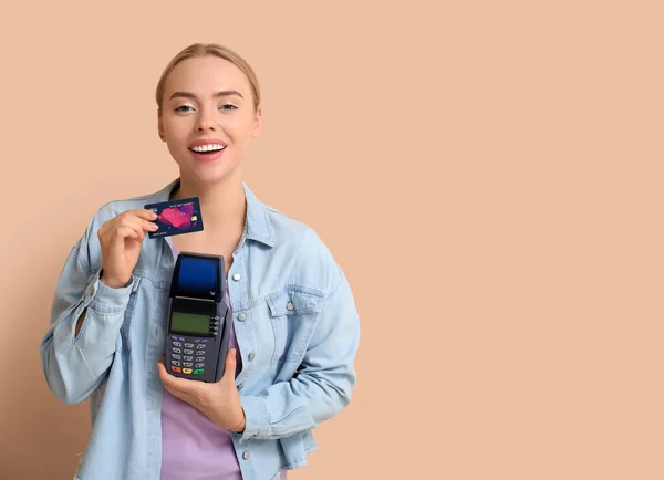 Pretty young woman with credit card and payment terminal on beige background