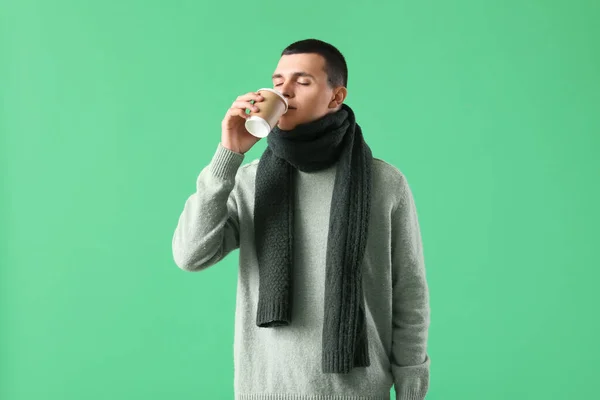 穿着冬衣的年轻人在绿色背景下喝咖啡 — 图库照片