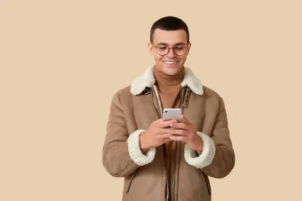 Young Man Sheepskin Jacket Using Mobile Phone Beige Background — Stock Photo, Image