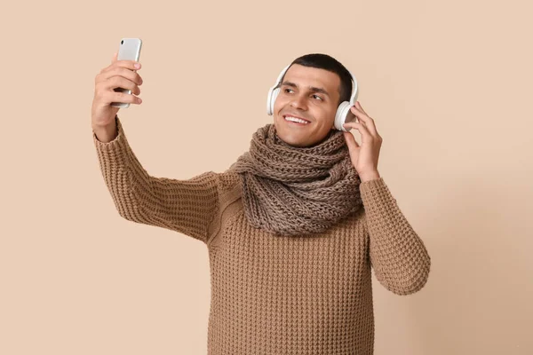 身穿冬季服装 头戴耳机 手持米色背景手机的年轻人 — 图库照片