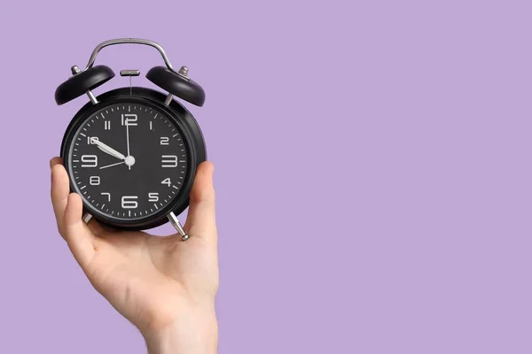 Male hand holding alarm clock on lilac background