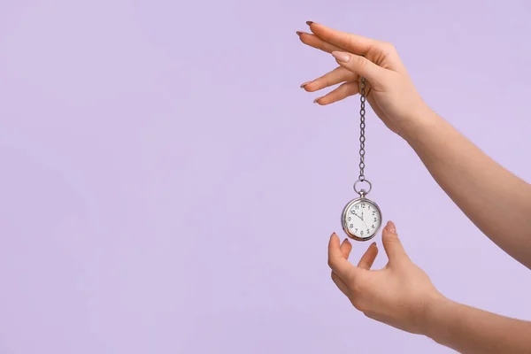 Female hands holding pocket watch on lilac background
