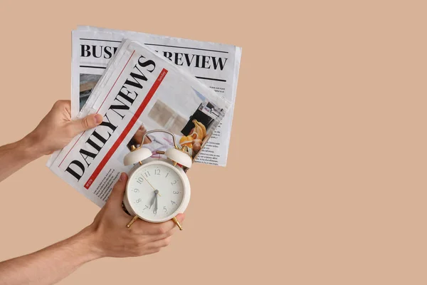 ベージュの背景に目覚まし時計や新聞を保持する男性の手 — ストック写真