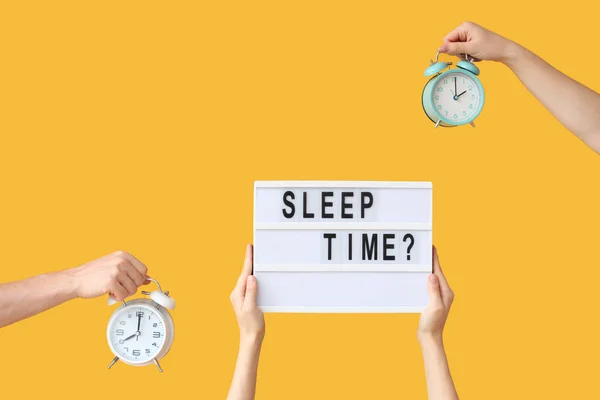 Hands holding alarm clocks and board with question SLEEP TIME? on yellow background