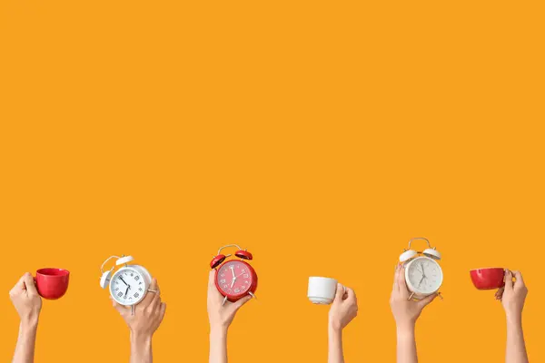 黄色の背景に異なる目覚まし時計とカップを保持する手 — ストック写真