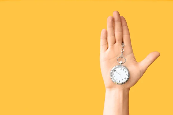 Female hand holding pocket watch on yellow background