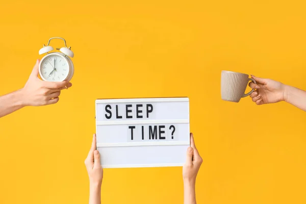 Hands holding alarm clock, cup and board with question SLEEP TIME? on yellow background