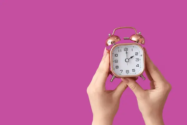 紫色の背景に目覚まし時計を保持する女性の手 — ストック写真