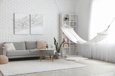 Hamağı, gri kanepesi ve kahve masası olan aydınlık oturma odasının içinde.