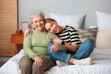 Büyükannesiyle yatak odasında kucaklaşan genç bir kadın.