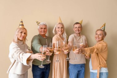 Turta ve şampanyayla olgun insanlar bej arka planda doğum gününü kutluyorlar.