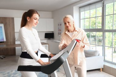 Rehabilitasyon merkezinde koşu bandında genç bir kadınla çalışan kadın fizyoterapist.