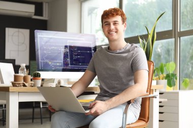 Erkek programcı ofiste dizüstü bilgisayarla çalışıyor.