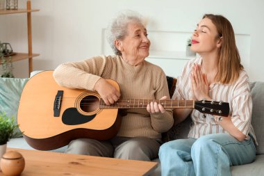 Genç kadın ve büyükannesi evde gitar çalıyorlar.