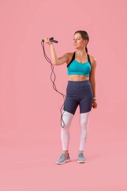 Pembe arka planda ip atlayan genç bir kadın.