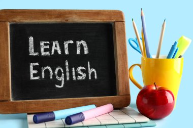 Kırtasiye malzemesi, taze elma ve mavi zemin üzerinde LeARN ENGLISH yazılı karatahta