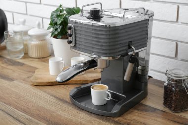 Modern coffee machine with cup of hot espresso on table in kitchen