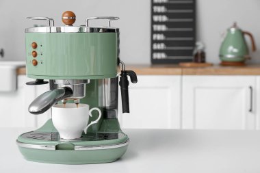 Modern coffee machine with cup of hot espresso on table in kitchen